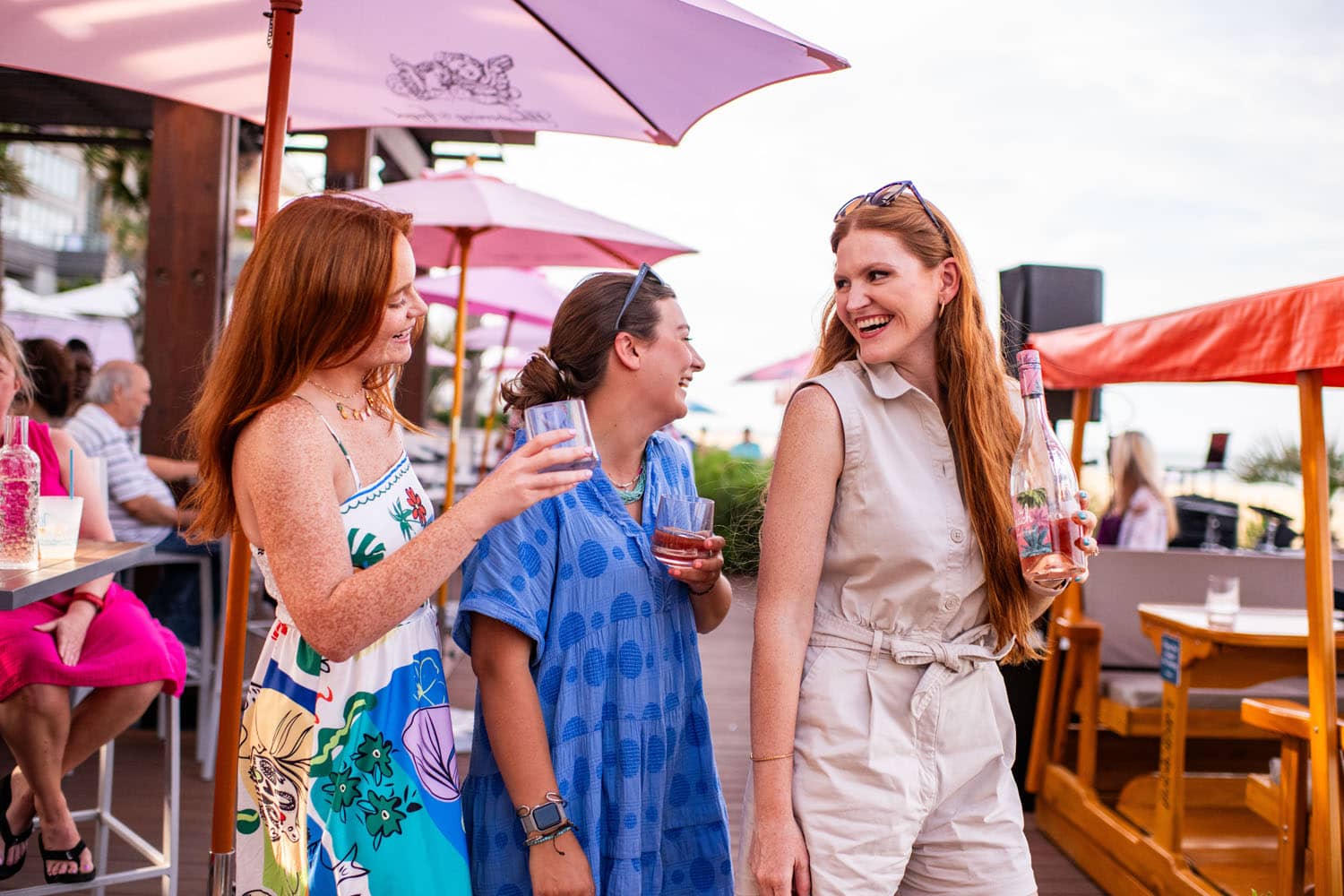 Three women holding drinks at an outdoor beach party