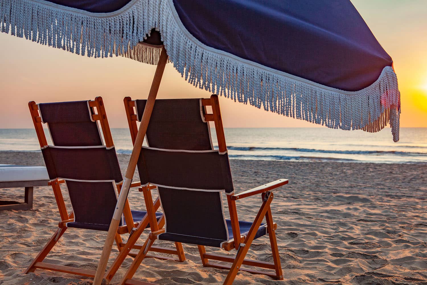 A pair of empty beach chairs on the beach at sunset
