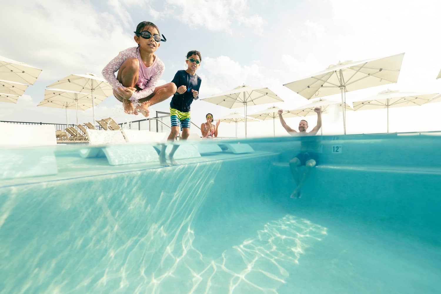 Two young children jumping into a pool with their parents watching them closely