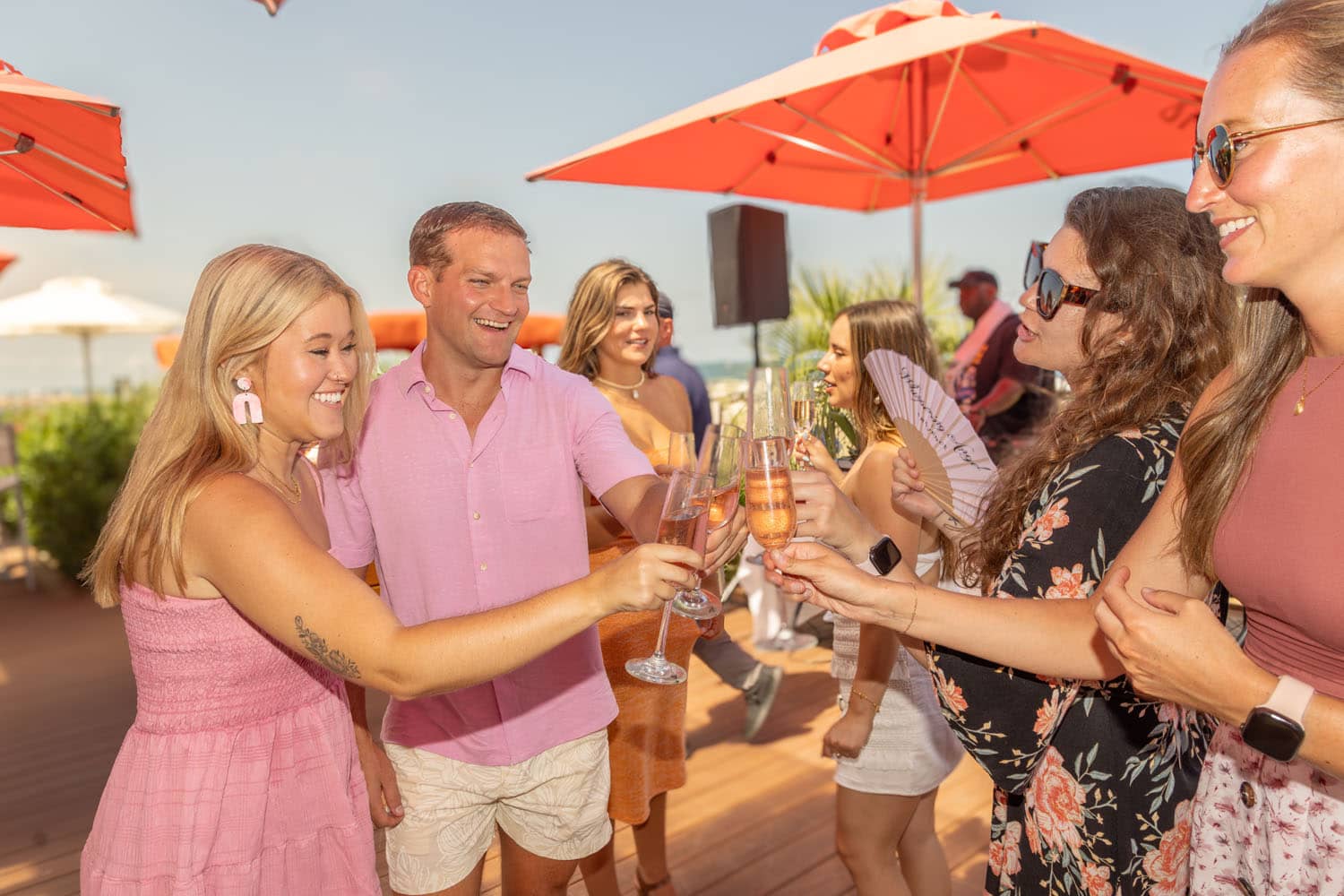 A group of friends dancing and drinking wine on an outdoor deck near the beach