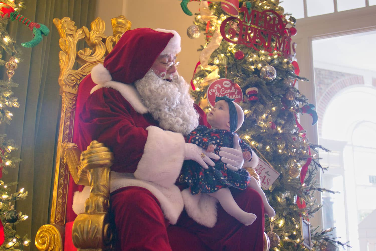 Santa posing for a photo with a baby inside a lobby
