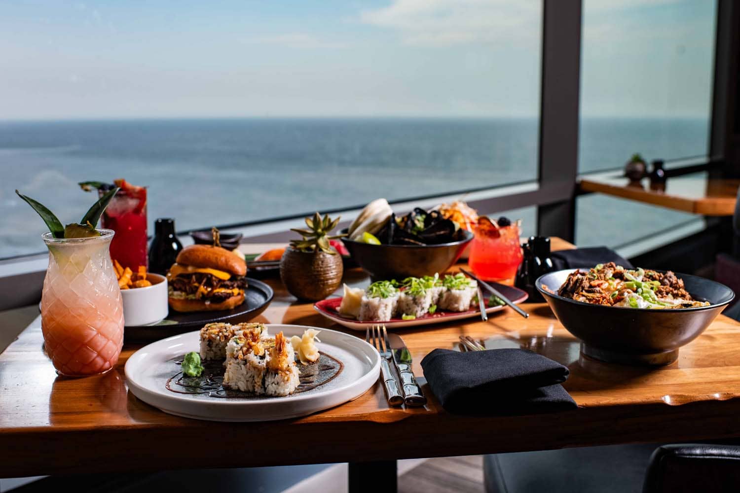 A variety of plated meals and drinks on a table at Orion's Roof restaurant with ocean views