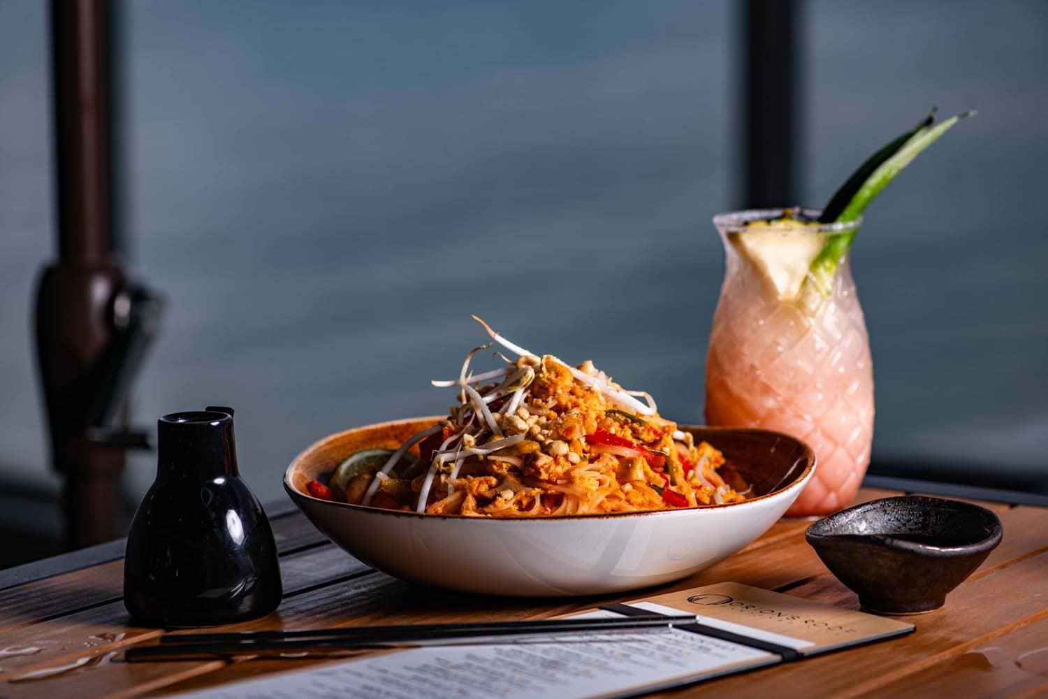 A pad Thai dish and drink on a table at Orion's Roof