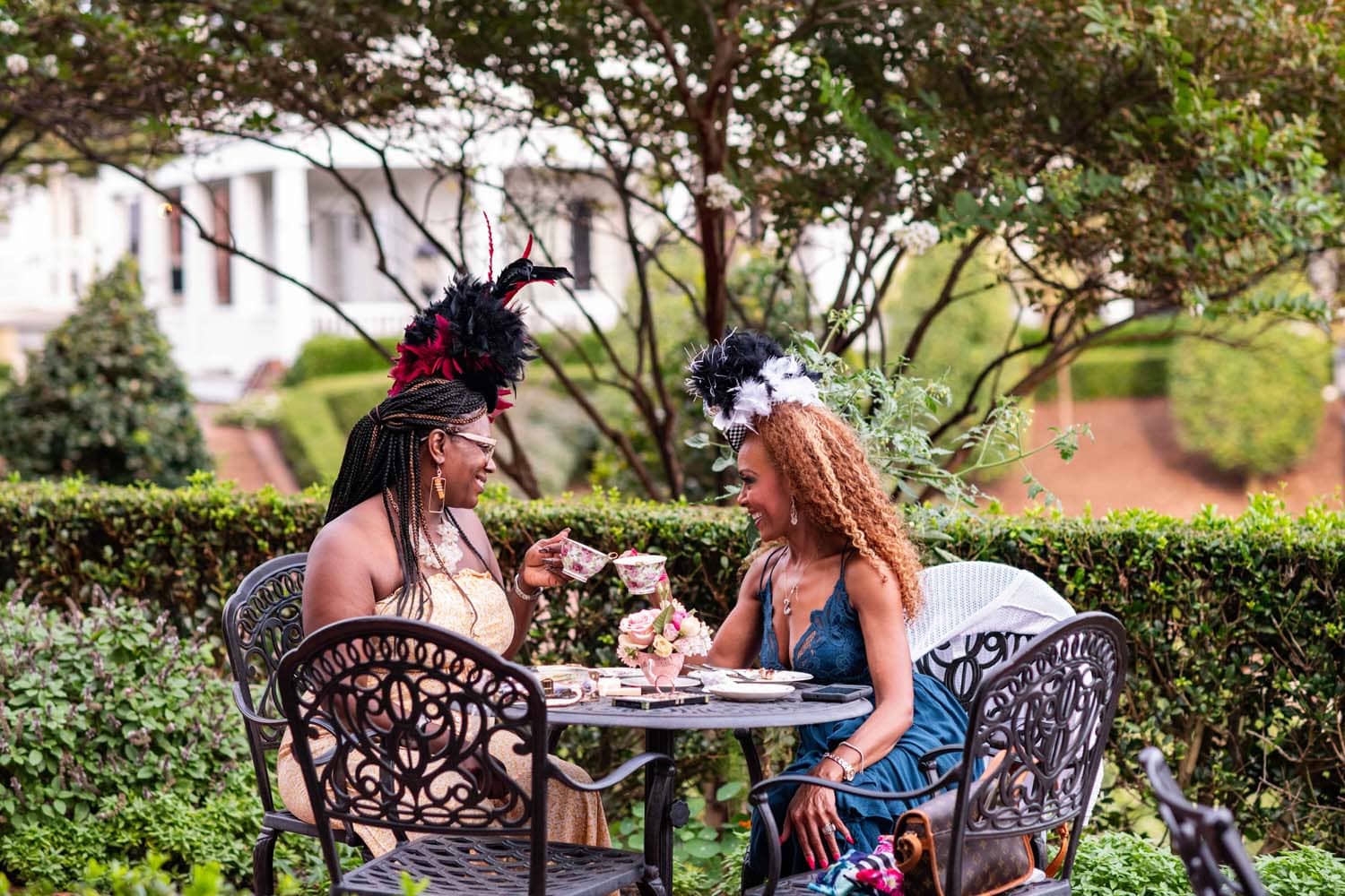 Two women drinking tea outside in a garden at a themed party