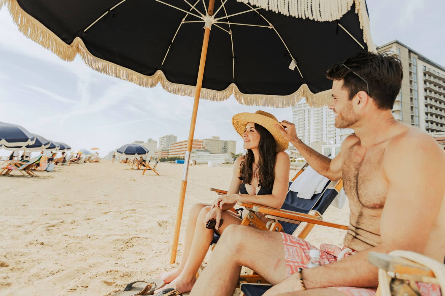 A couple sitting on chairs under an umbrella on the beach